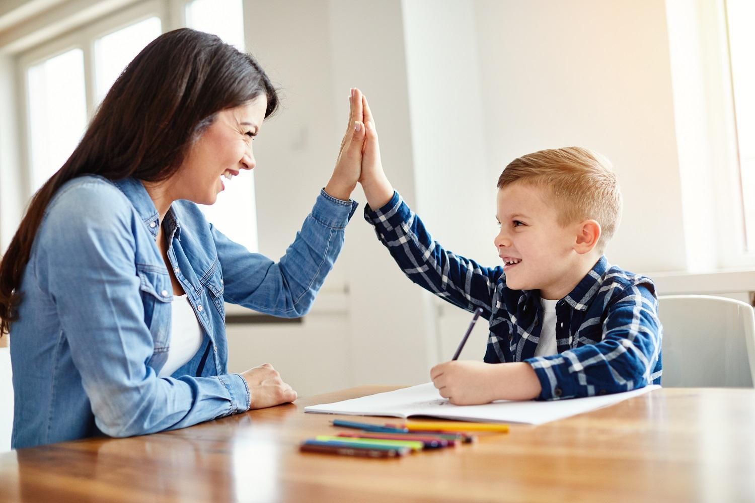 Unsere Kita (c) istockphoto.com Junge und Erzieherin sitzen am Tisch und klatschen ab