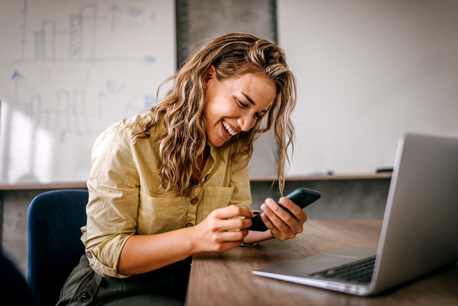 Frau sitzt lächelnd am Handy, vor ihr steht ein geöffneter Laptop auf dem Tisch (c) istockphoto.com Frau sitzt lächelnd am Handy, vor ihr steht ein geöffneter Laptop auf dem Tisch