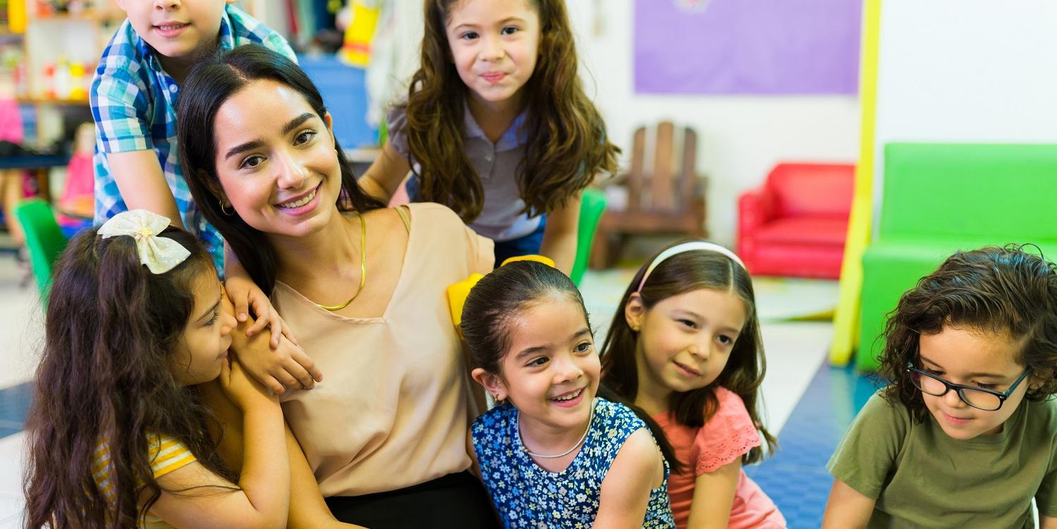 Junge Erzieherin, die in einer Gruppe von Kindern sitzt. Alle lächeln. (c) istockphoto.com Junge Erzieherin, die in einer Gruppe von Kindern sitzt. Alle lächeln.