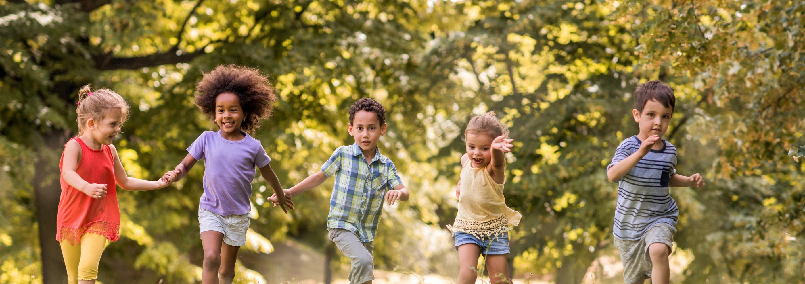 Man sieht lachende Kinder, die über eine Wiese laufen und sich dabei an den Händen halten