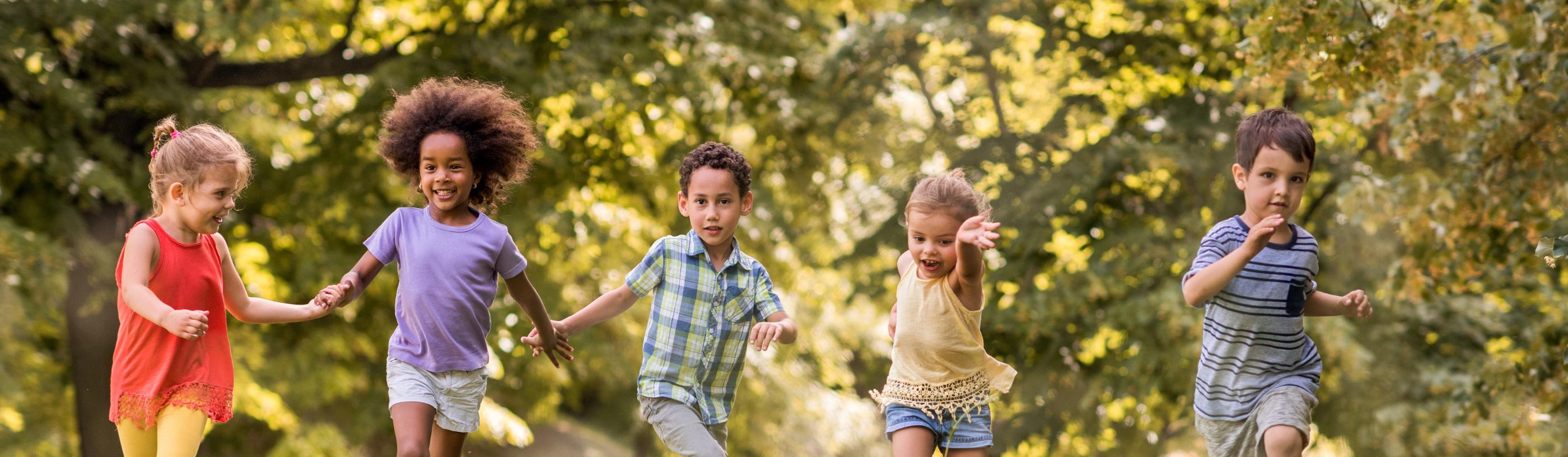Man sieht lachende Kinder, die über eine Wiese laufen und sich dabei an den Händen halten
